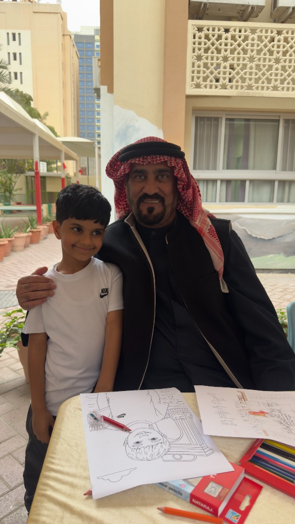 طفل مع كبير بالزي التقليدي أثناء نشاط تلوين خارجي يعزّز الترابط والانتماء