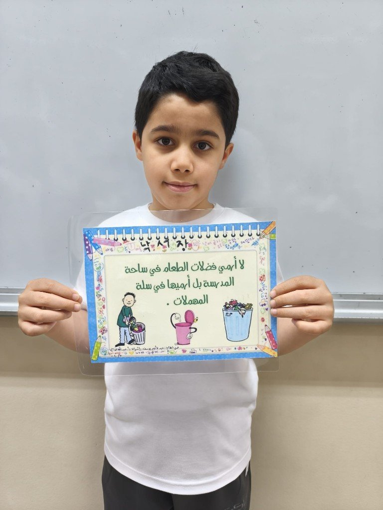 الطالب عبدالأمير يوسف يعرض لافتة: عدم رمي فضلات الطعام في الساحة واستخدام سلة المهملات