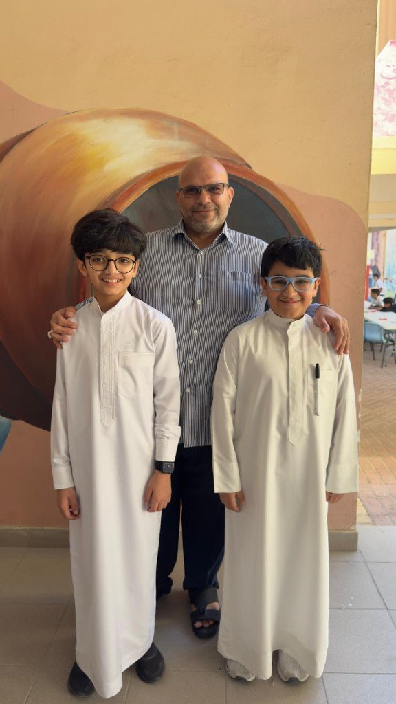 أ. عبدالله ضاحي مع طالبين أمام جدارية في فضاء مدرسي