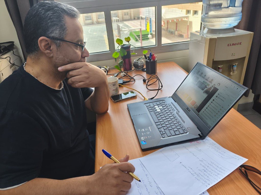 أ. ياسر العلويات أثناء العمل على الحاسوب والتوثيق في مكتب مضيء بضوء النهار